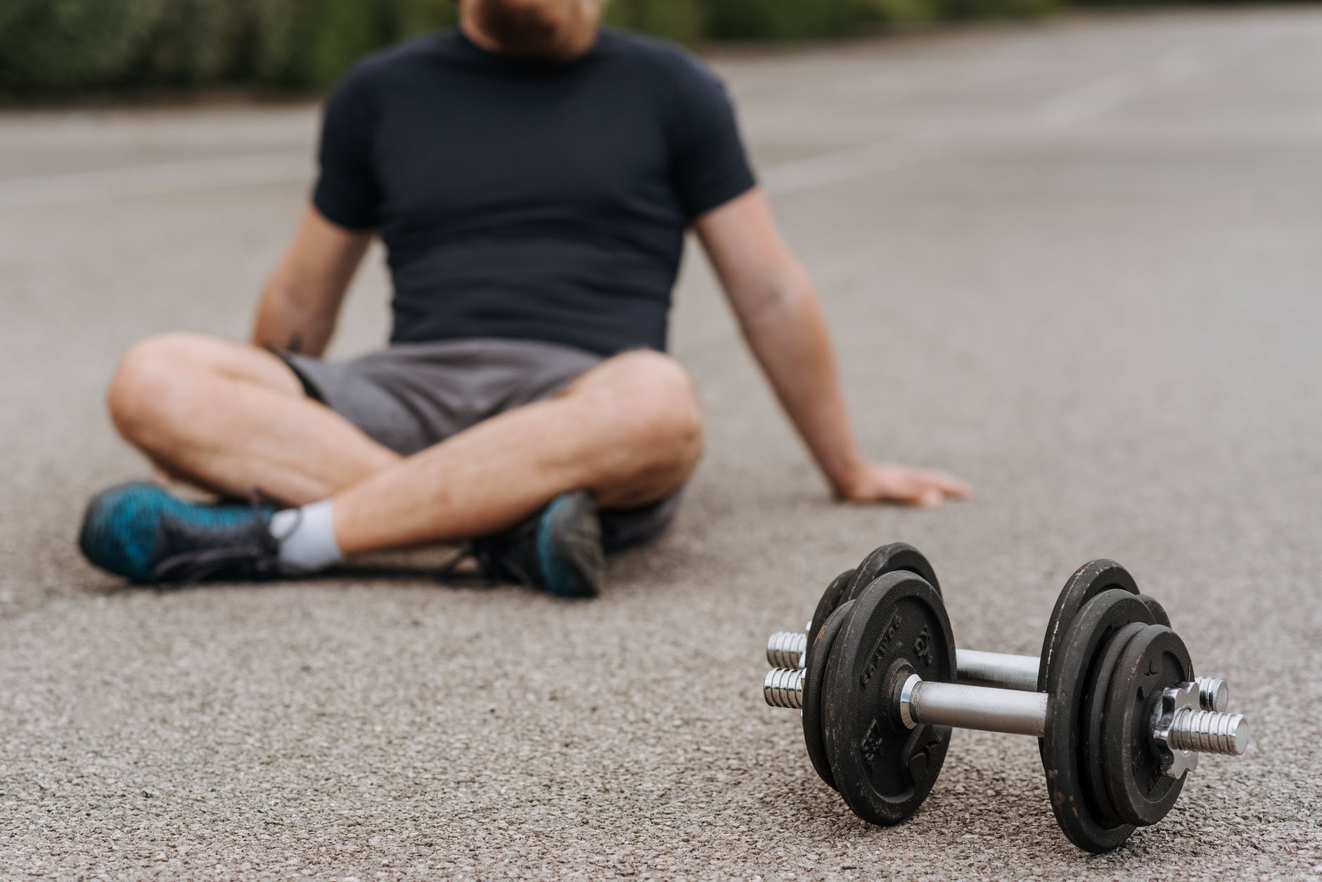 crop sportsman resting on road near dumbbells after working out
